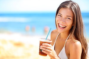 A woman happily holds a drink on the beach